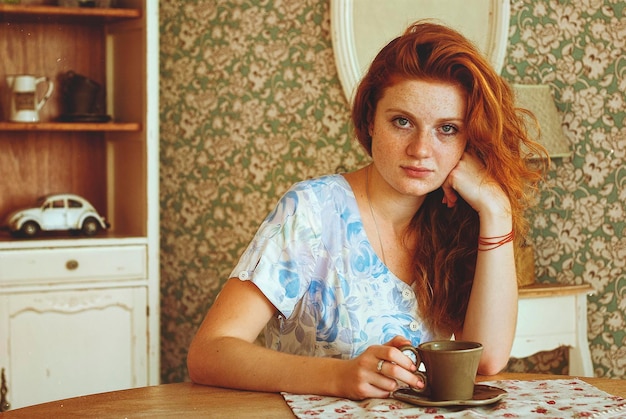 retrato de mulher jovem e bonita com cabelo cacheado ruivo e olhos azuis contra fundo cinza.