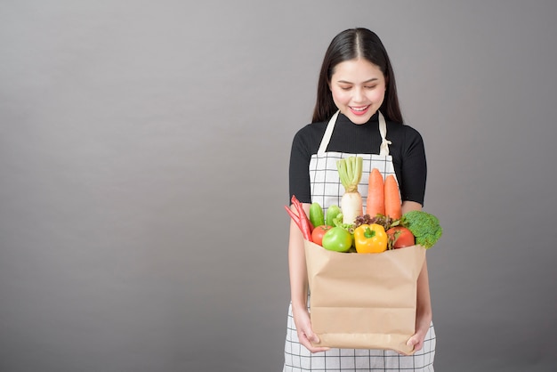 Retrato de mulher jovem e bonita com legumes na sacola de compras em fundo cinza studio