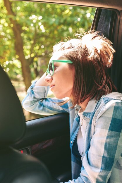 Retrato de mulher jovem e bonita com óculos de sol, olhando a paisagem pela janela do carro em um dia ensolarado