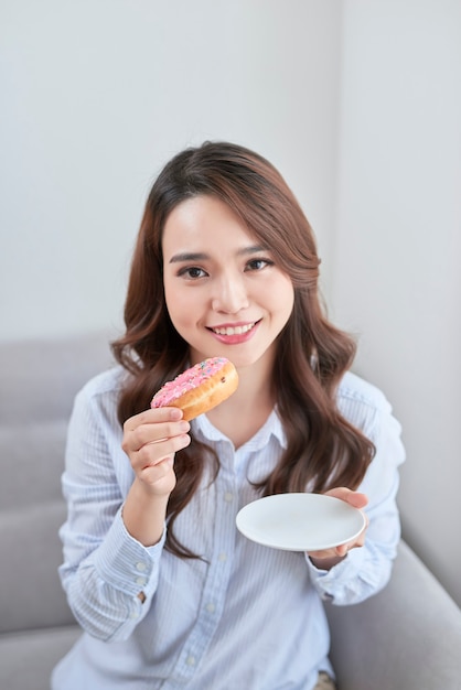 Retrato de mulher jovem e bonita comendo donuts em casa.