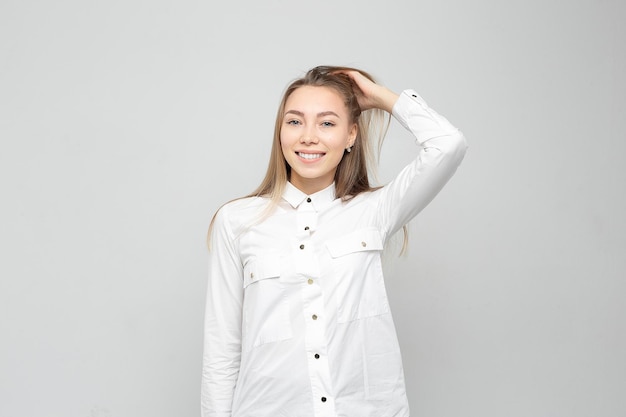 Retrato de mulher jovem e bonita Retrato de uma bela loira sorridente na camisa branca em uma mulher branca e grisalha endireita o cabelo ou segura a cabeça