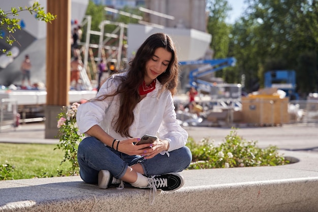 Retrato de mulher jovem e bonita usando seu celular na rua