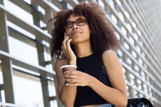 Retrato de mulher jovem e bonita usando seu telefone celular na rua.