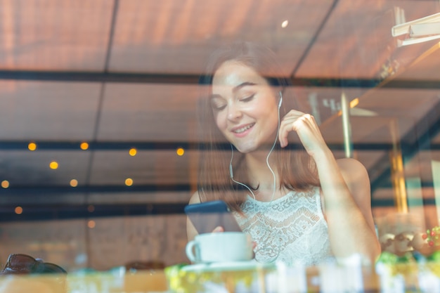 Retrato de mulher jovem feliz com caneca nas mãos, bebendo café no restaurante