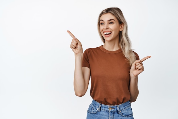 Retrato de mulher jovem feliz, sorrindo, apontando o dedo para o lado e olhando para a esquerda em uma das opções em branco