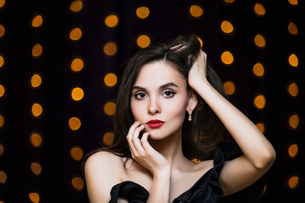 Foto retrato de mulher jovem morena linda e luxuosa em fundo de luzes douradas.