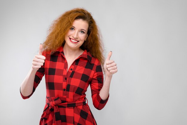 Retrato de mulher jovem ruiva bonita feliz sorrindo com polegares para cima em fundo cinza