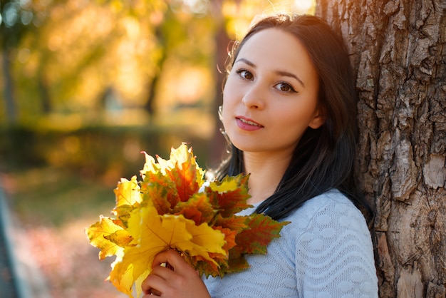 Retrato de mulher jovem sorridente com Outono folhas na frente de folhagem