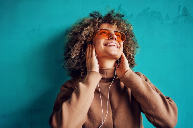 Retrato de mulher jovem sorridente elegante com cabelo encaracolado, ouvir música e desviar o olhar.