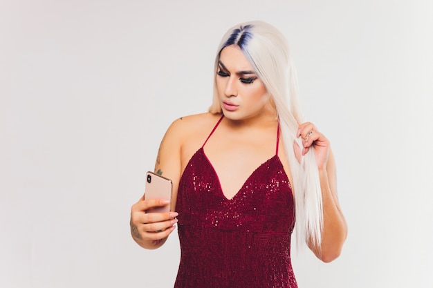 Retrato de mulher jovem trans no vestido vermelho com lantejoulas, olhando para o smartphone