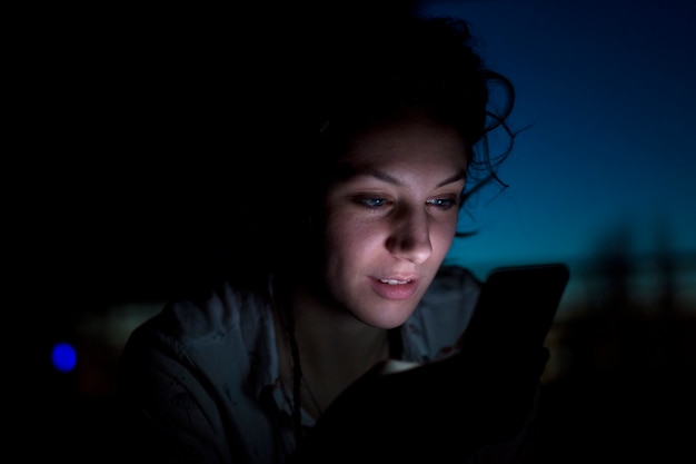 Retrato, de, mulher jovem, usando, telefone móvel, tarde à noite