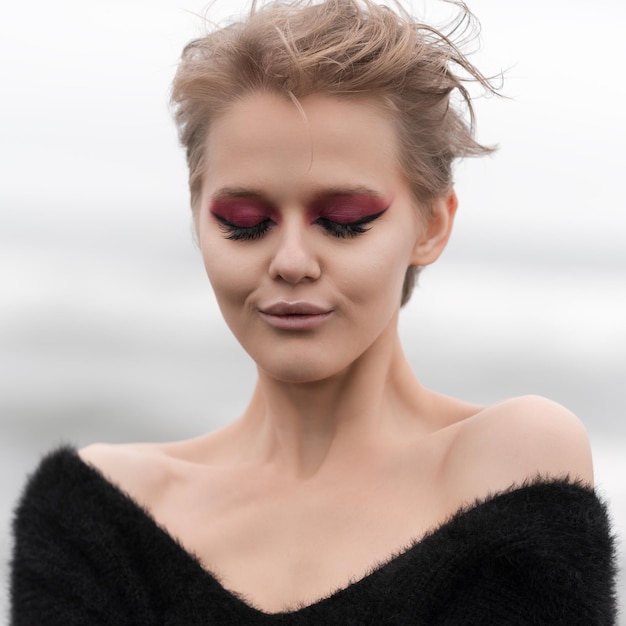 Retrato de mulher loira com cabelo curto e maquiagem brilhante posando ao ar livre com os olhos fechados