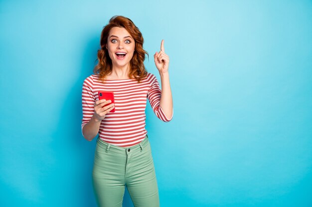 Retrato de mulher louca animada usando tipo de celular postagem do blog Pense pensamentos têm uma ideia incrível grite uau omg levante o dedo indicador, use um casaco da moda isolado sobre a cor azul