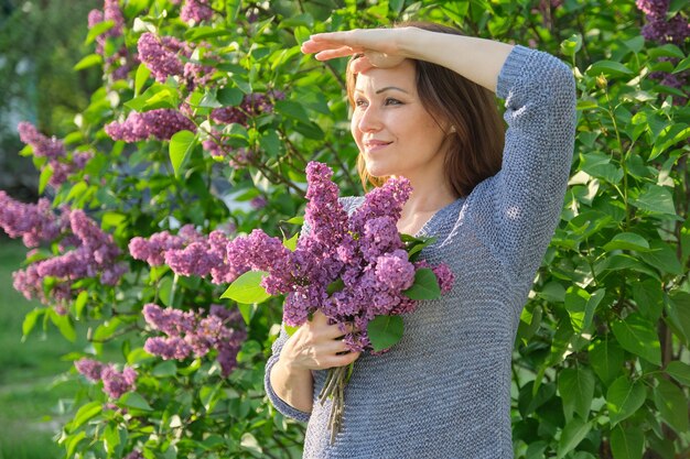 Retrato de mulher madura sorridente no jardim com buquê de lilases