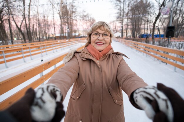 Retrato de mulher madura sorrindo para a câmera e segurando as mãos do marido durante o passeio na pista de patinação