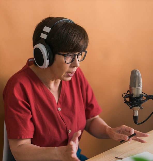 Retrato de mulher madura usando fones de ouvido e falando em podcast de estação de rádio online e conceito de transmissão