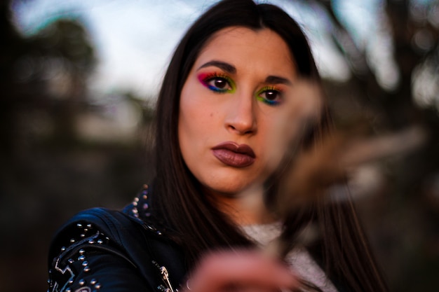 Retrato de mulher maquiada com uma folha ao pôr do sol, observando a natureza