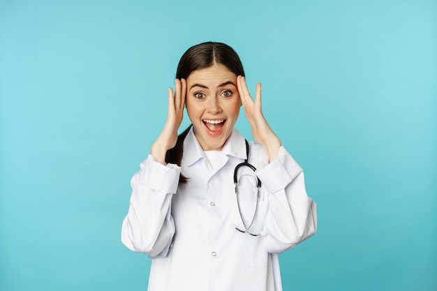 Retrato de mulher médica sorridente surpresa e animada segurando as mãos na cabeça reação a alucinante...