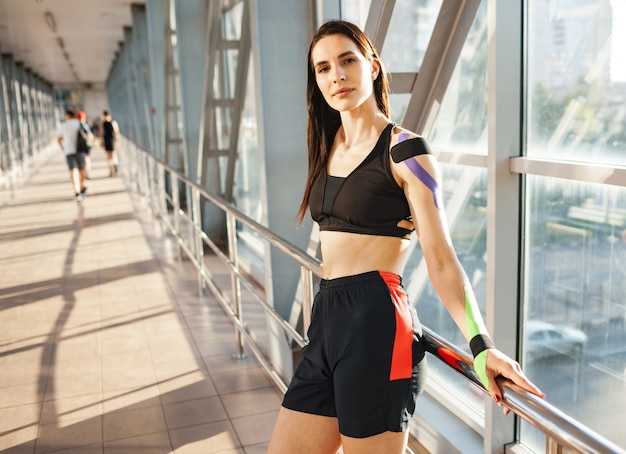 Retrato de mulher morena musculosa usando roupa esportiva preta, olhando para a câmera