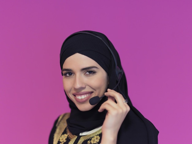 retrato de mulher muçulmana com cachecol hijab representante do cliente mulher de negócios com fone de ouvido telefone ajudando e apoiando on-line com o cliente no call center moderno isolado no fundo rosa
