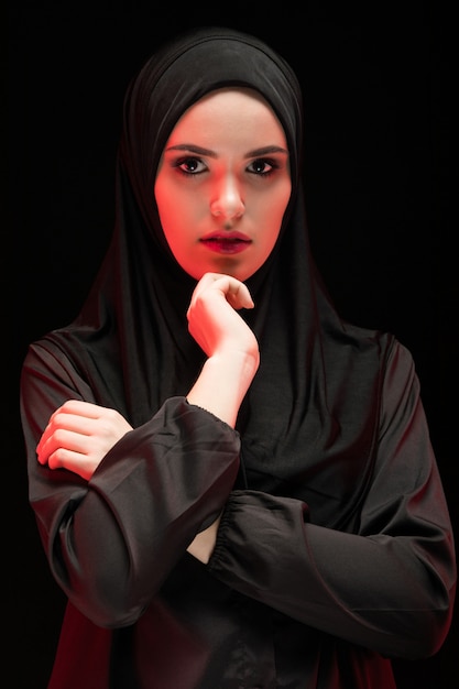 Retrato de mulher muçulmana séria jovem bonita vestindo preto hijab como conceito de moda conservadora com a mão perto do rosto em preto