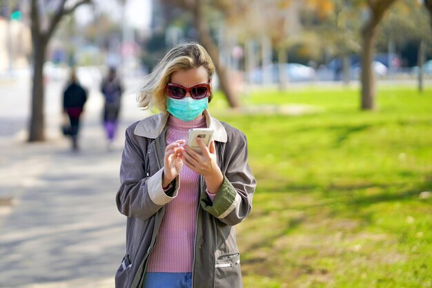 Retrato de mulher na rua em uma máscara médica e fala ao telefone. Modelo infeliz atraente com gripe ao ar livre.