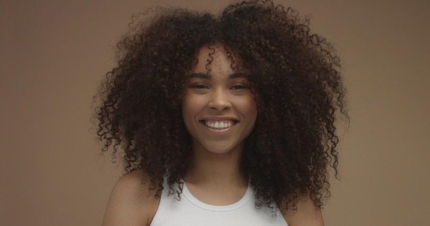 Retrato de mulher negra de raça mista com grande cabelo encaracolado afro em fundo bege