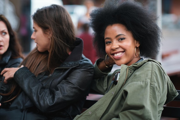 Retrato de mulher negra e amigos ao ar livre com comunicação em um banco urbano Grupo de mulheres felizes e conversa de um jovem com um sorriso feliz sentindo-se relaxado com fundo desfocado