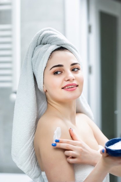 Retrato de mulher no banheiro aplicando creme hidratante no banheiro após o banho