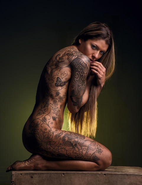 Foto retrato de mulher nua com tatuagem sentada junto à parede