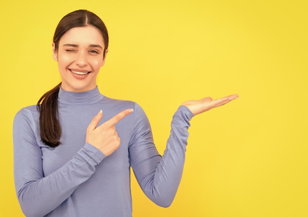 Retrato de mulher piscando, aponte os dedos no espaço da cópia, publicidade de fundo amarelo