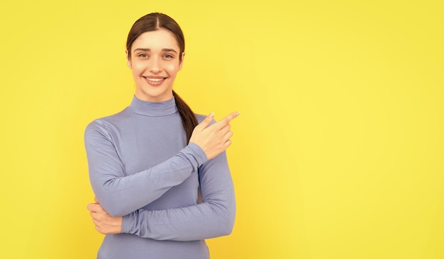 Retrato de mulher positivo apontando dedos no espaço de cópia amarelo fundo mostrando