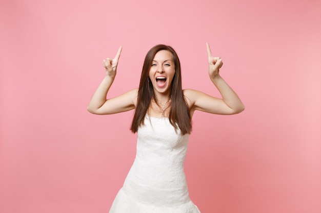 Retrato de mulher radiante em um lindo vestido branco em pé e apontando o dedo indicador para cima