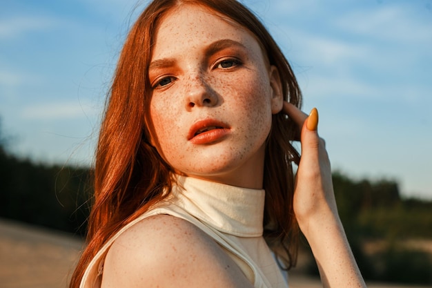 Retrato de mulher ruiva com sardas tocando cabelo e olhando para a câmera