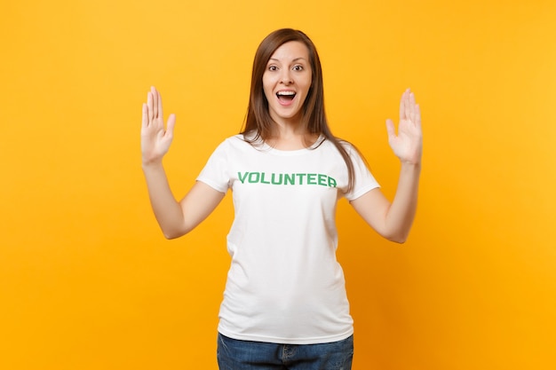 Retrato de mulher satisfeita sorridente feliz em camiseta branca com voluntário de título verde de inscrição escrita isolado em fundo amarelo. ajuda de assistência gratuita voluntária, conceito de trabalho de graça de caridade.