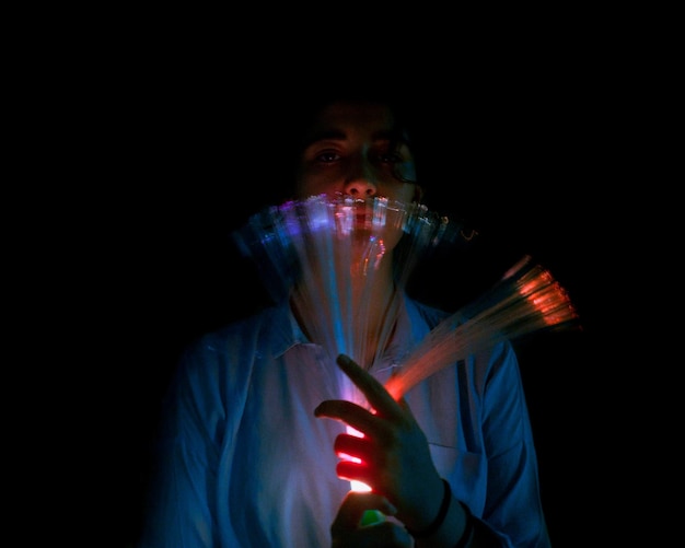Foto retrato de mulher segurando equipamentos de iluminação iluminados contra um fundo preto