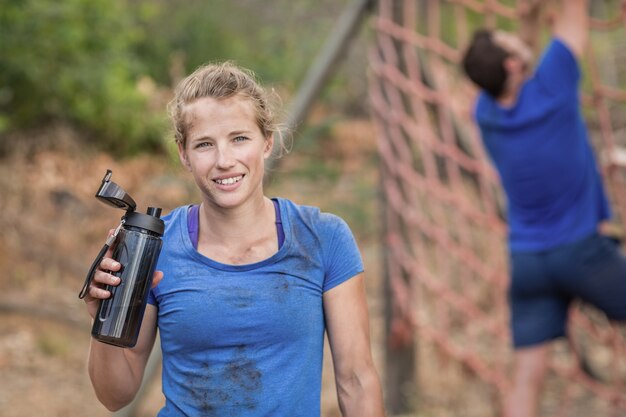 Retrato de mulher segurando uma garrafa de água durante a pista de obstáculos no campo de treinamento