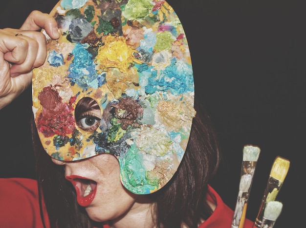 Foto retrato de mulher segurando uma paleta multicolorida pelo rosto contra um fundo preto