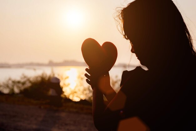 Foto retrato de mulher segurando uma planta de silhueta contra o céu durante o pôr do sol