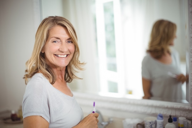 Retrato de mulher sênior segurando a escova de dentes no banheiro