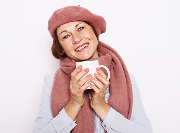 Retrato de mulher sênior usando chapéu rosa e cachecol com xícara de café