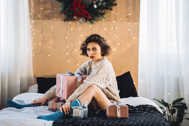 retrato de mulher sentada na cama com presentes por perto