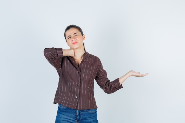 Retrato de mulher sentindo dor no pescoço, espalhando a palma da mão para o lado em uma camisa marrom listrada e parecendo incomodada com a vista frontal