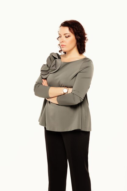 Retrato de mulher séria em uma blusa cinza posando em pé com os braços cruzados e olhando para baixo