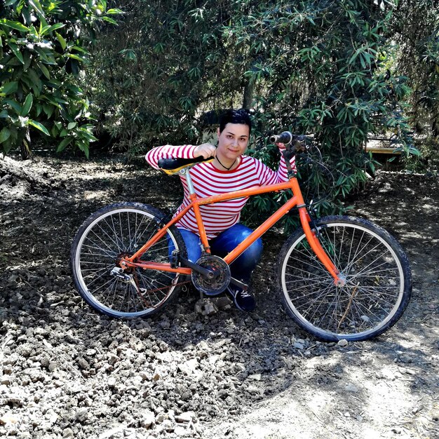 Foto retrato de mulher sorridente agachada em bicicleta no chão contra as árvores