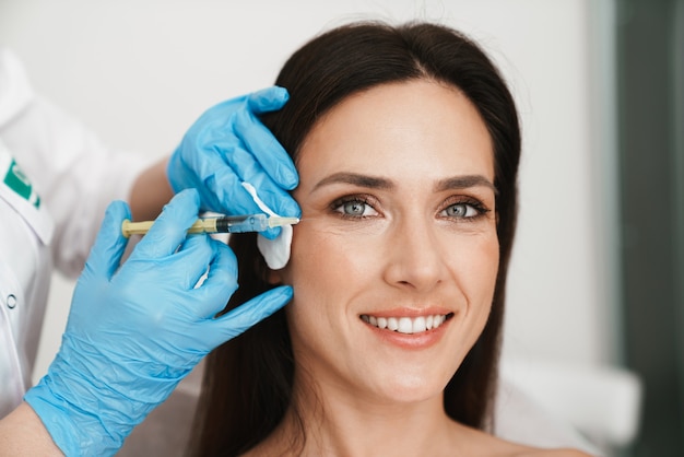 Retrato de mulher sorridente recebendo tratamento de mesoterapia no rosto por especialista em luvas em salão de beleza