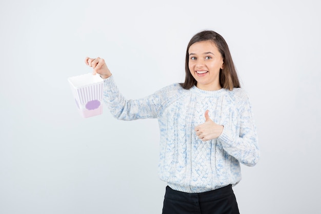 Retrato de mulher sorridente, segurando a caixa de pipoca e dando polegares para cima.