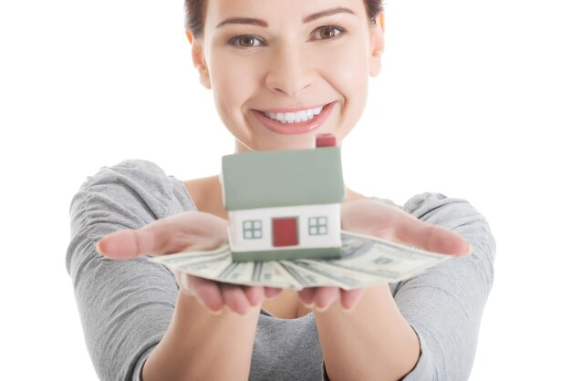 Foto retrato de mulher sorridente segurando papel moeda e casa modelo contra fundo azul