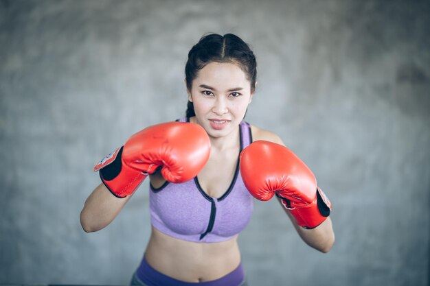 Retrato de mulher sorridente usando luvas de boxe enquanto está de pé no ginásio