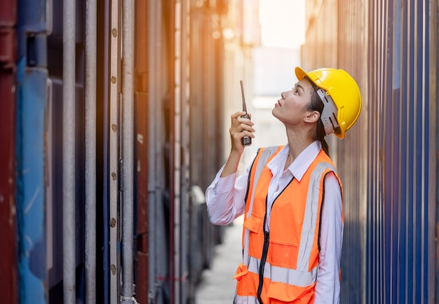 retrato de mulher trabalhadora asiática com uniforme de segurança, falando com walkie-talkie no armazém de contêiner.